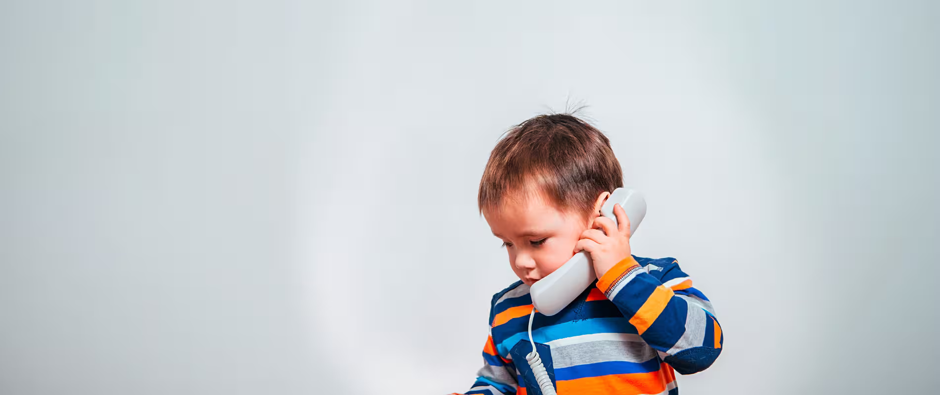 Kind hält einen Telefonhörer ans Ohr – Symbolbild für Kontakt, Beratung und Unterstützung für Familien